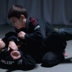Crianças vestidas com quimonos praticam jiu-jitsu em uma sessão de treino sobre o tatame.