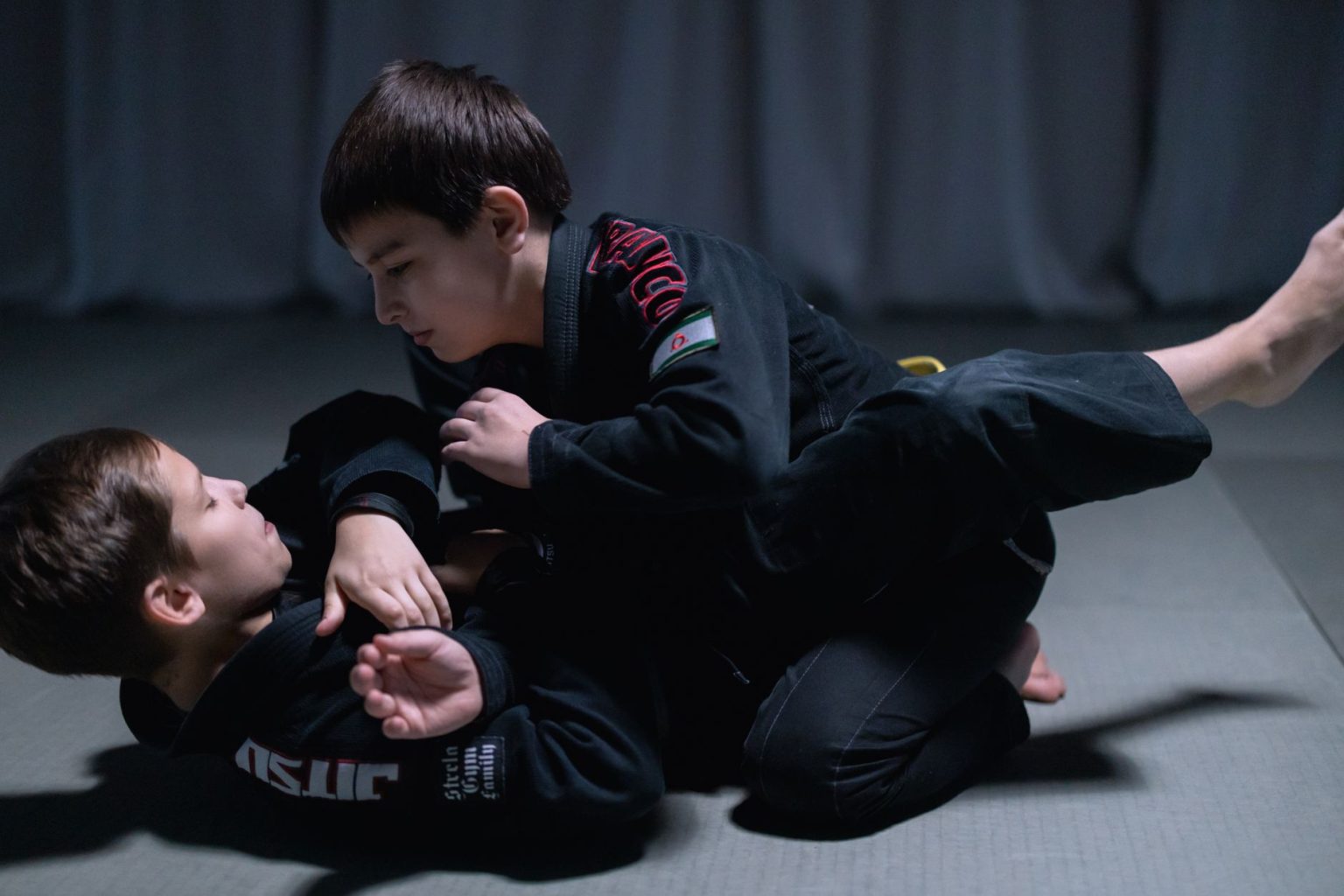 Crianças vestidas com quimonos praticam jiu-jitsu em uma sessão de treino sobre o tatame.