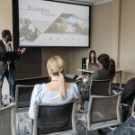 Participantes acompanham uma apresentação sobre negócios em uma sala de conferências.