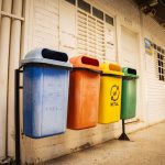 Quatro lixeiras para diferentes tipos de materiais dispostas em um espaço urbano, destacando a separação de resíduos.