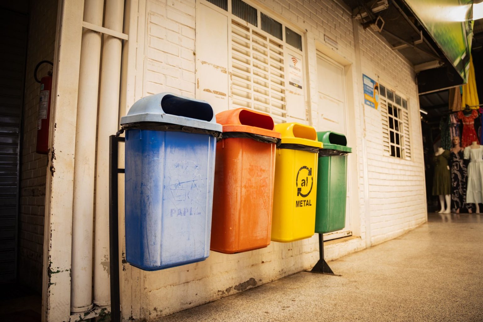Quatro lixeiras para diferentes tipos de materiais dispostas em um espaço urbano, destacando a separação de resíduos.