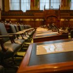 Interior de uma câmara legislativa vazia, com fileiras de mesas e microfones.