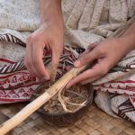 Mãos de artesão trabalhando com madeira e fibras naturais em um ambiente tradicional.