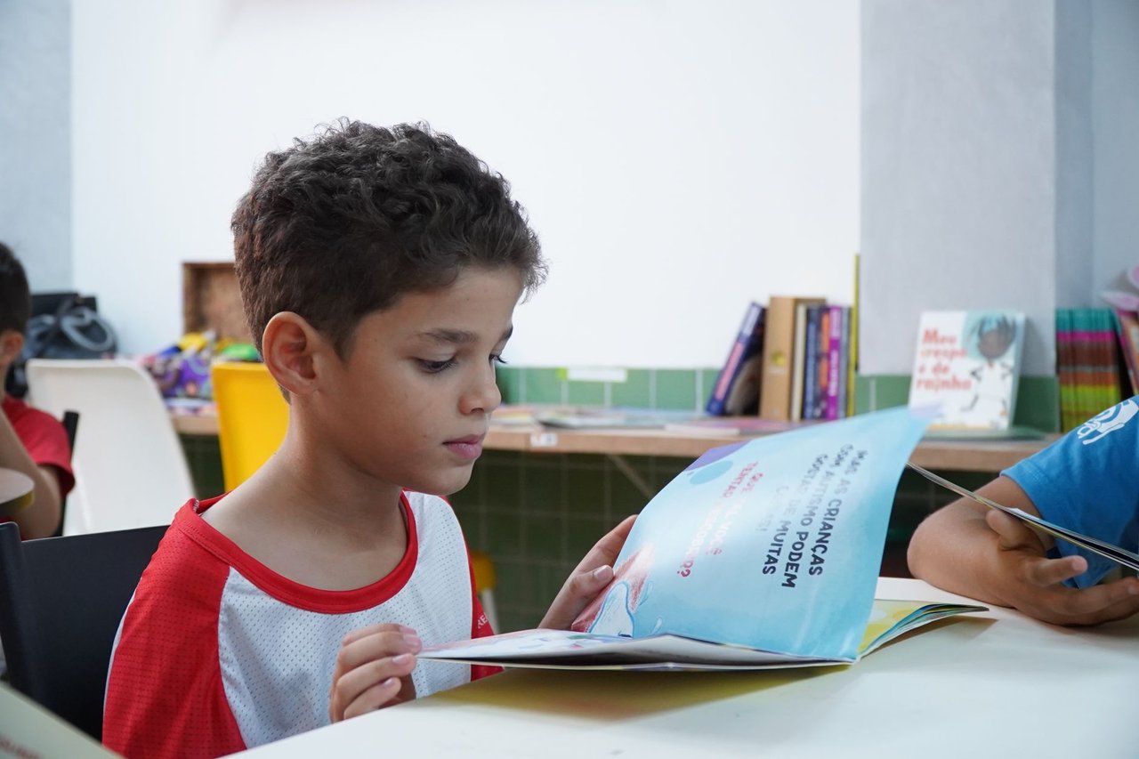 Menino lê atentamente um livro em uma sala de aula.