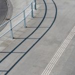 Vista aérea de uma calçada urbana com corrimãos metálicos e piso tátil para acessibilidade.