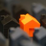 Miniaturas de casas, com uma residência laranja em destaque entre modelos pretos, representando a avaliação de imóveis.