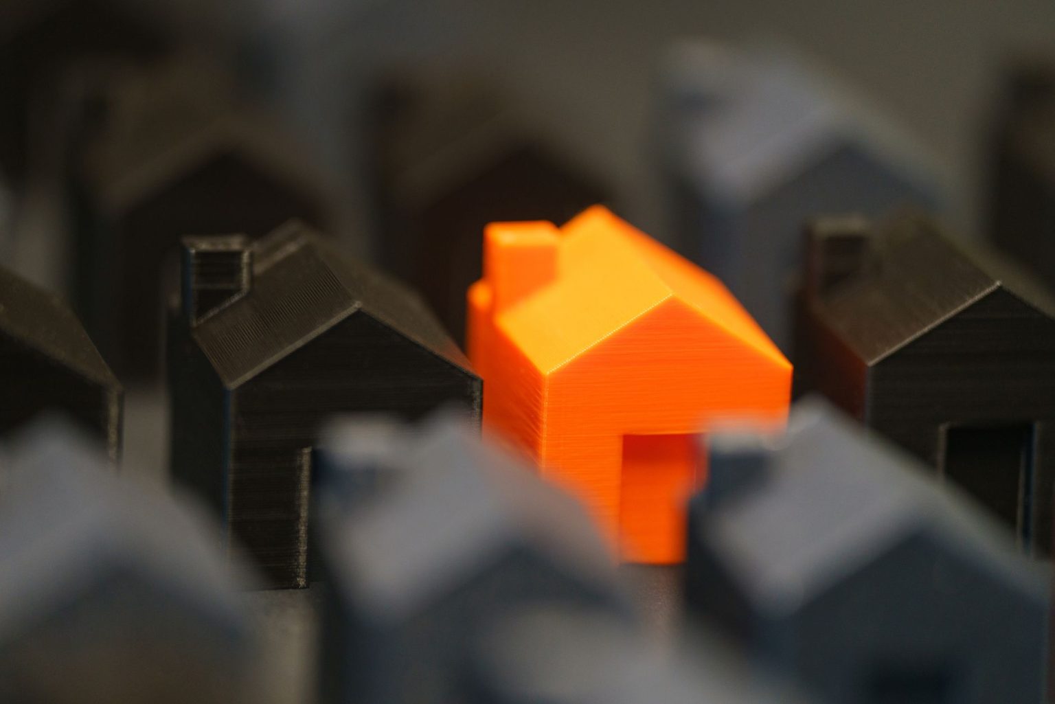 Miniaturas de casas, com uma residência laranja em destaque entre modelos pretos, representando a avaliação de imóveis.