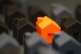 Miniaturas de casas, com uma residência laranja em destaque entre modelos pretos, representando a avaliação de imóveis.