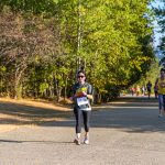 Grupo de mulheres correndo em uma estrada arborizada durante uma prova esportiva.