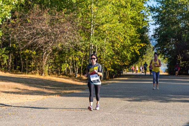 Grupo de mulheres correndo em uma estrada arborizada durante uma prova esportiva.